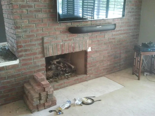 An older brick fireplace and chimney breast inside a living room before the work began.