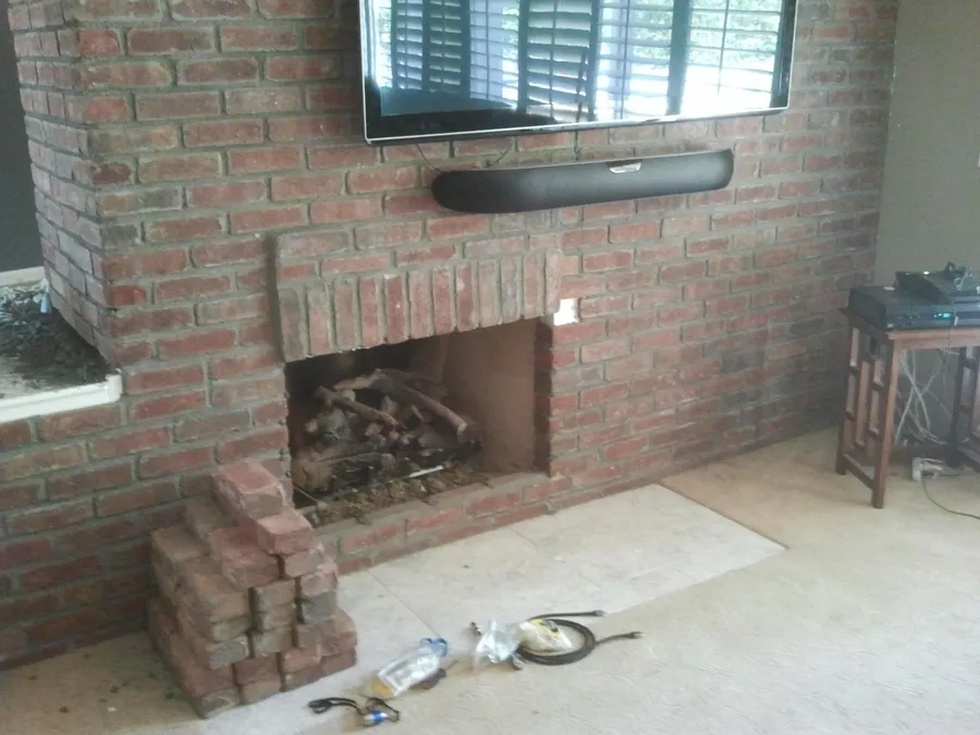 Brick fireplace and hearth mid-restoration, with salvaged replacement bricks stacked ready for repointing.