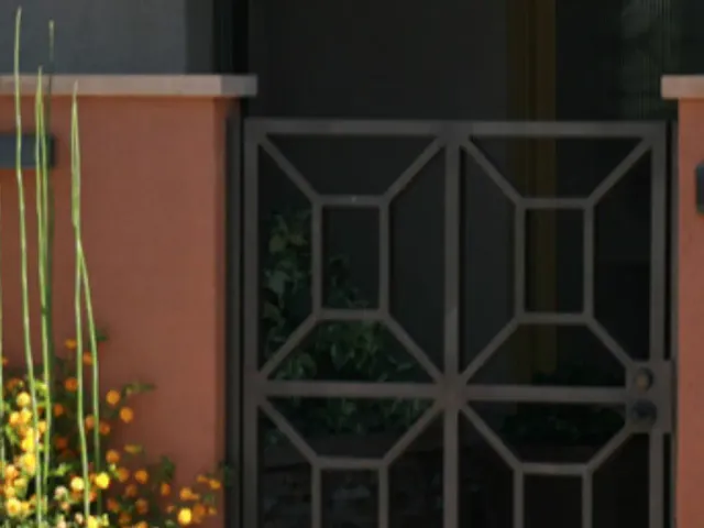 Stucco masonry pilasters framing a black wrought-iron entry gate.
