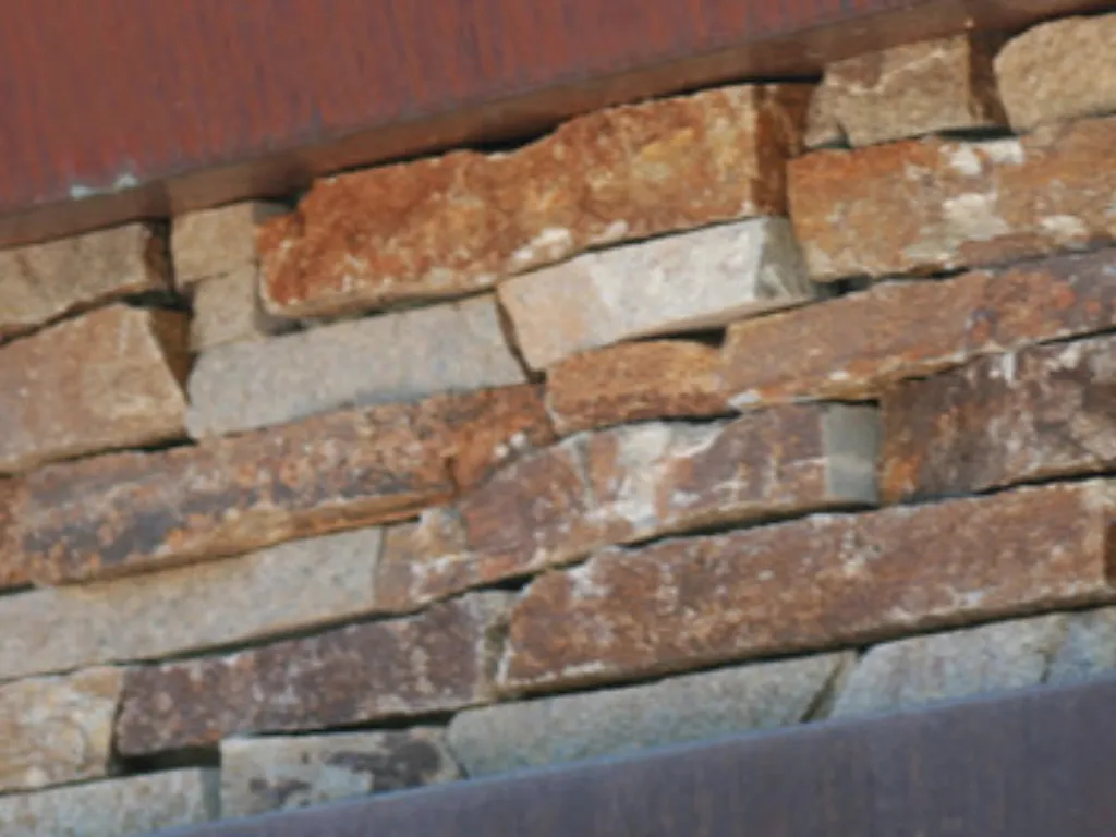 Close-up of dry-stacked ledgestone veneer in warm tan and rust tones, fitted tight beneath a timber sill.