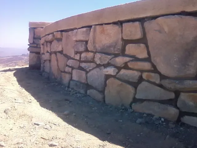 Hand-set natural rock wall with mortared joints along a dry slope.