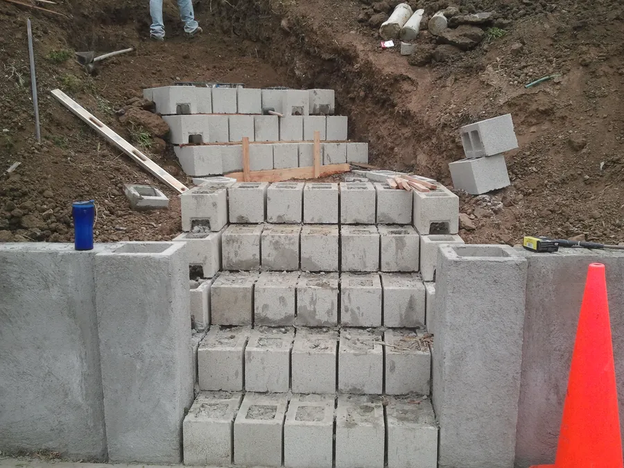 Concrete block stair and walls under construction, stepping up into an excavated slope.