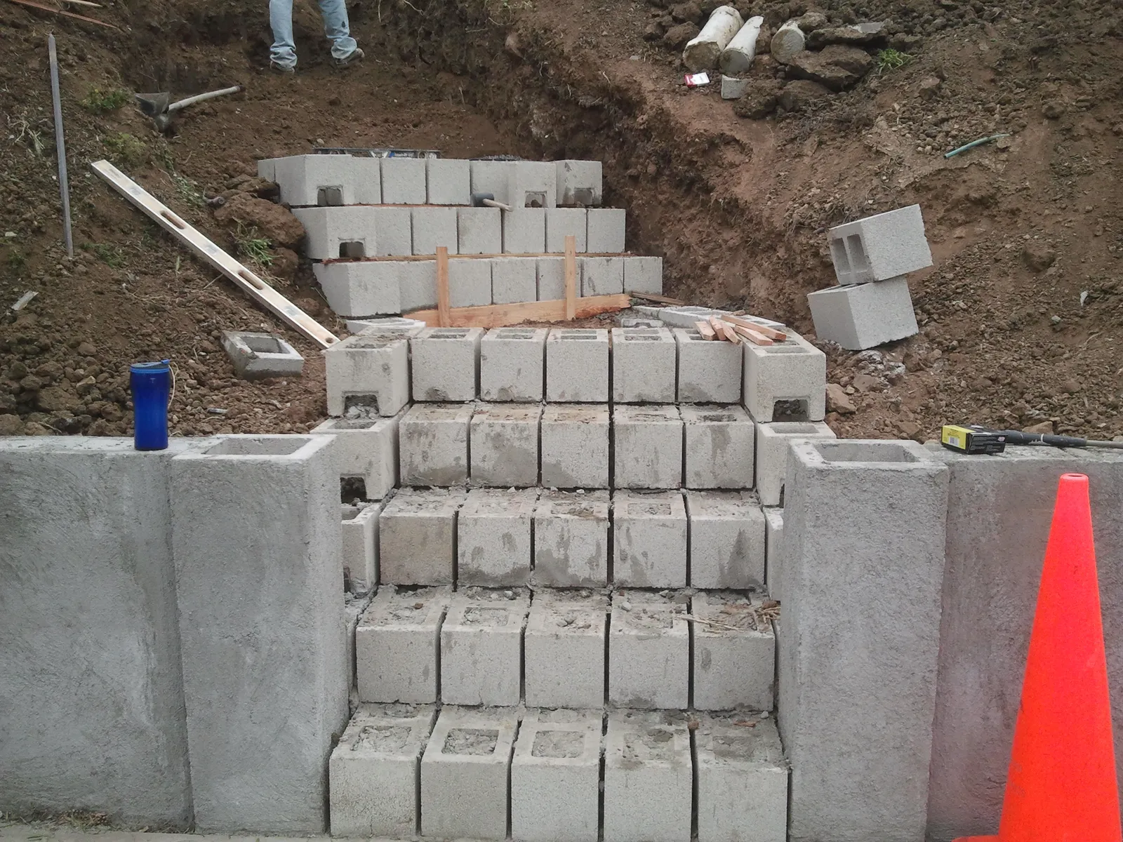 Concrete block stair and stepped retaining walls being built into an excavated San Diego hillside, with a new block wall along the street.