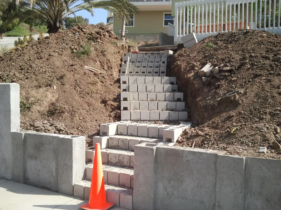 Concrete block stair rising up the cut slope between new retaining walls.