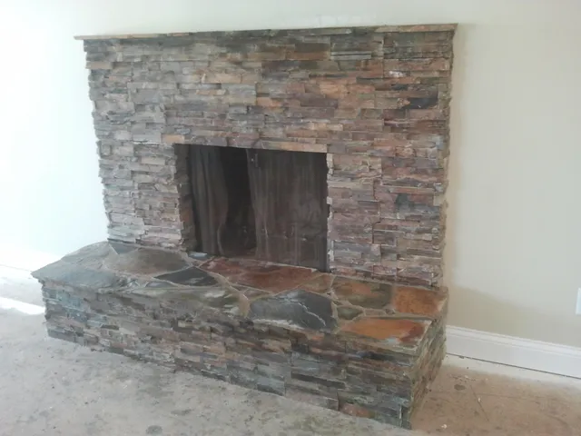 A finished floor-to-ceiling stacked-stone fireplace with a raised hearth.