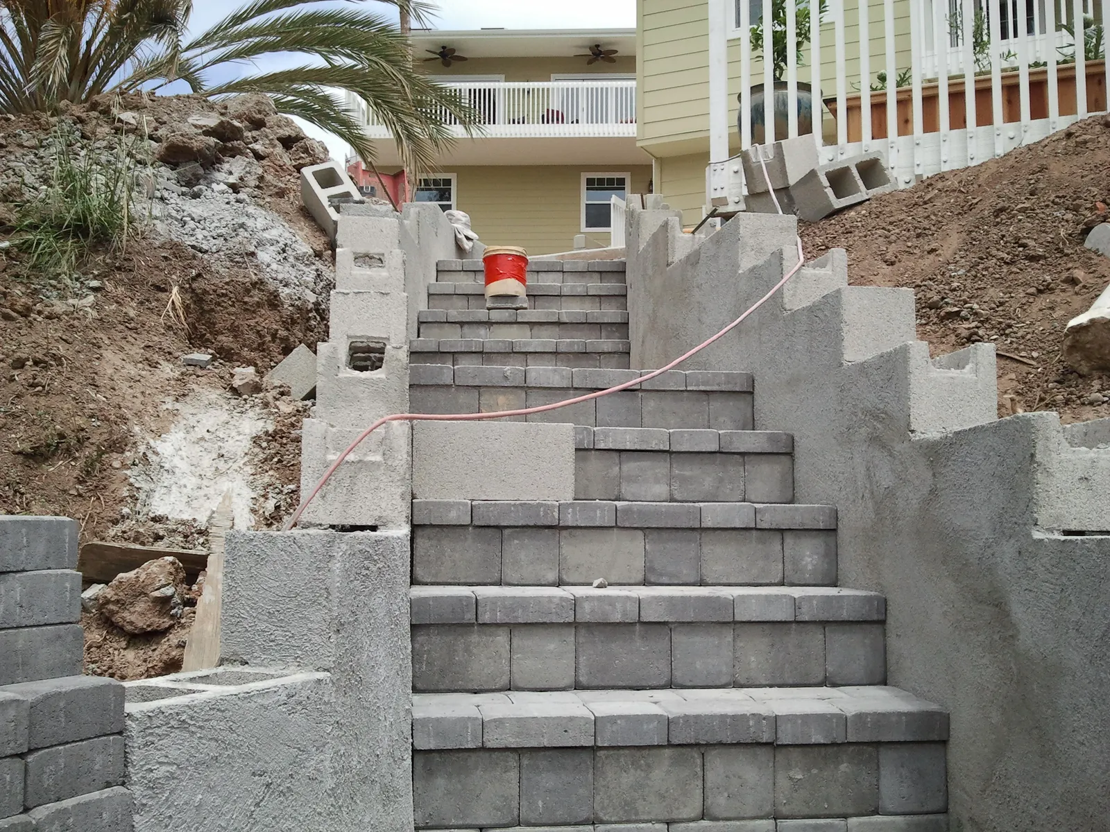 Paver stairway climbing between stepped concrete block walls on a hillside lot, mid-construction.