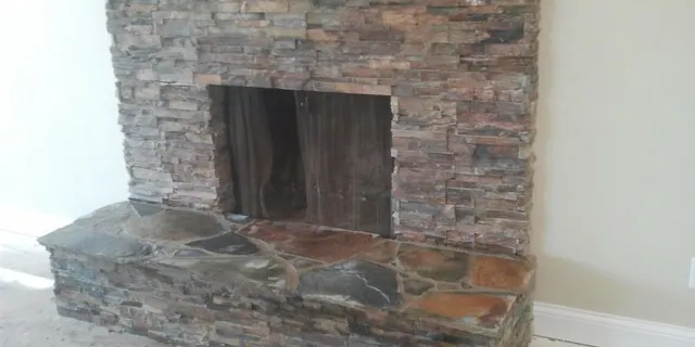 A stacked-stone fireplace wall with a raised stone hearth, seen from an angle.