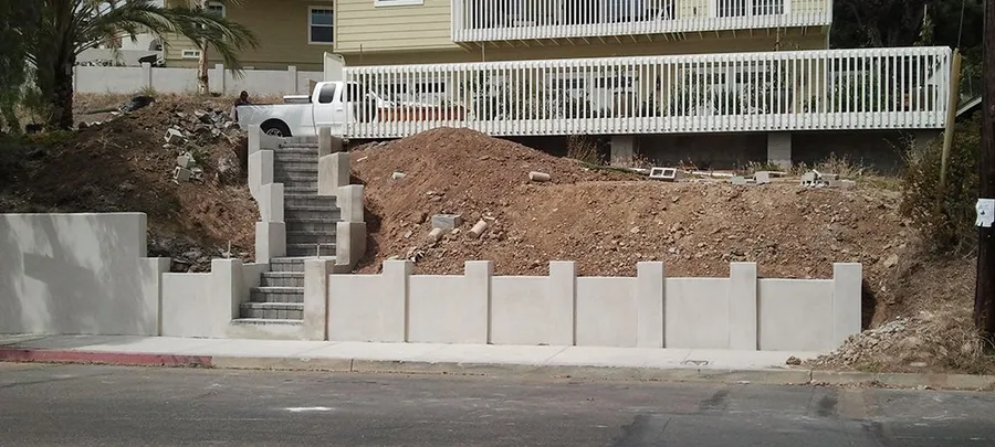 Finished street-front wall with pilasters and a paver stairway, with new sidewalk and curb below.