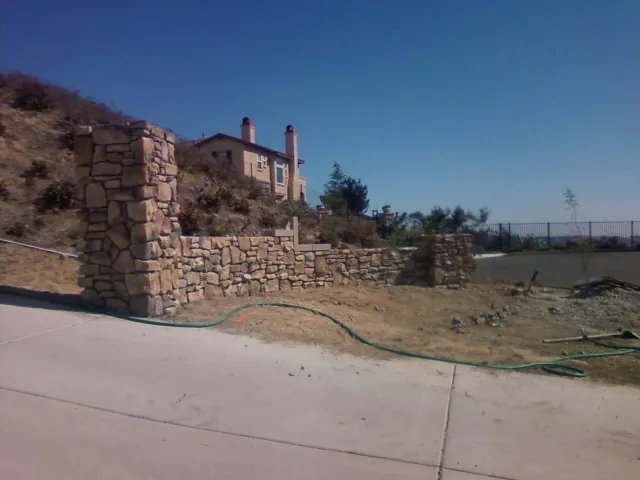 Stone pillar and low wall at a concrete driveway entrance.