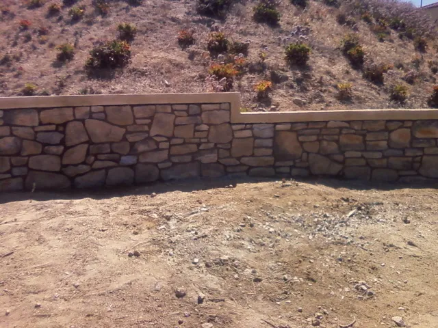 Finished stone veneer retaining wall with a mortar cap along a dry hillside.