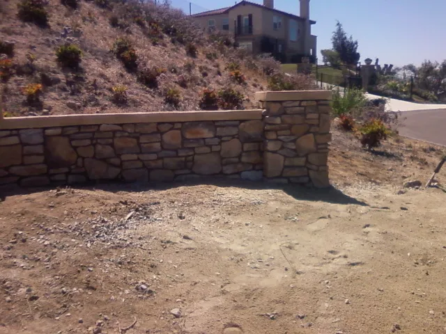 Finished stone wall ending in a stone pillar at the driveway.