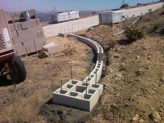Concrete block wall core laid on a new footing along a hillside driveway, before its stone facing.