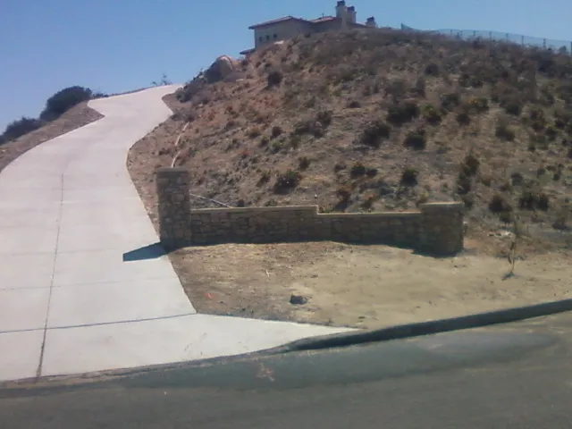 Finished stone wall and pillar at the foot of a long hillside driveway.